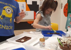 Na zdjęciu widoczny jest chłopiec i dziewczynka ozdabiający swoje czekolady.