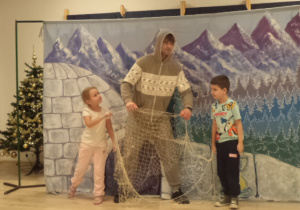 Aktor ubrany w zimowy kombinezon, wraz z dziewczynką i chłopcem trzymają sieć.