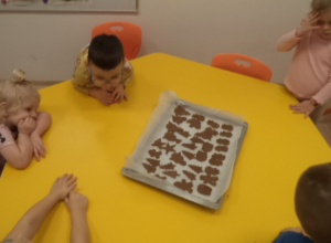 Na zdjęciu widać leżącą na stole tacę z pierniczkami, której przyglądają sie dzieci.