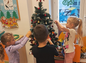 Dwie dziewczynki i chłopiec ubierają choinkę.
