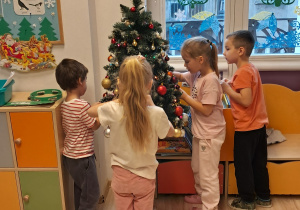 Dwóch chłopców i dwie dziewczynki ubierają choinkę.