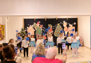 Dzieci z grupy Motylków tańczą w rytm znanej piosenki "Let It Snów" z wykorzystaniem niebieskich pomponów symbolizujących śnieżki.