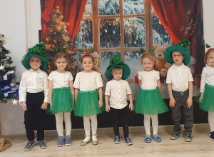 Dzieci ubrane na galowo z zielonymi elementami pozują na tle świątecznej dekoracji.