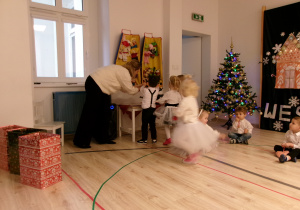Na zdjęciu widać jak dzieci razem z panią ubierają choinkę.