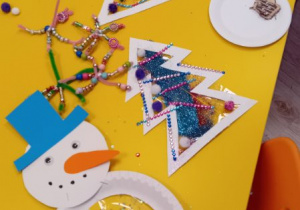 Na zdjęciu widać prace dzieci - bałwanki i choinki zrobione z papierowych talerzyków i folii.