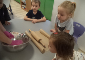 Na zdjęciu widać dzieci, które przyglądają się jak pani wyrabia ciasto.