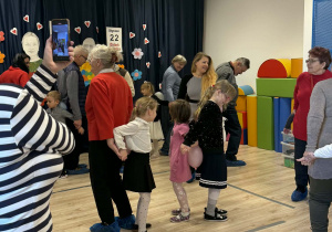 Na zdjęciu widać Babcie i Dziadków wraz z ich wnukami, którzy wspólnie tańczą z balonem.