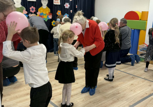 Na zdjęciu możemy dostrzec Babcie i Dziadków wraz z ich wnukami, którzy wspólnie tańczą trzymając balon.