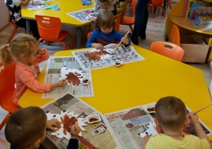 Dzieci siedzą przy stolikach i malują wycięte z papieru jeże.