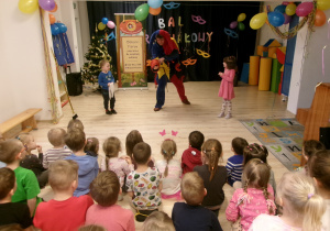 Na zdjęciu widać dzieci siedzące na sali. Dwójka dzieci pomaga magikowi w przedstawieniu.