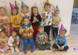 Na zdjęciu widać dzieci ubrane w kolorowe urodzonowe czapeczki, trzymające małe prezenciki.