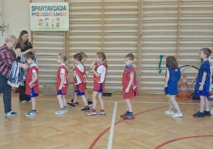 Na zdjęciu widać dzieci stojące w rzędzie, czekajace na otrzymanie medalu.