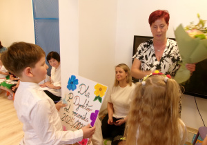 Na zdjęciu widać parę dzieci wręczających pani Dyrektor kwiaty oraz prezent.