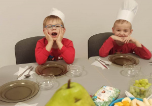 Dzieci siedzą przy stoliku. Pani nauczycielka pokazuje im jak wygląda gruszka.