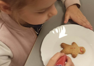 Dziewczynka, za pomocą pisaka spożywczego, ozdabia ciastko w kształcie ludzika.