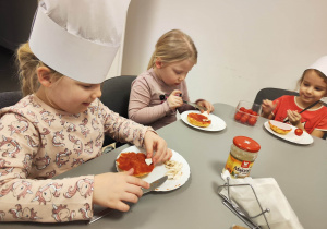 Dziewczynki układają na bułkach kawałki pomidorów.