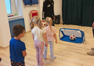 Na zdjęciu widoczny jest piłkarz z Łódzkiego Klubu Sportowego oraz troje dzieci, które strzelają gole do bramki.