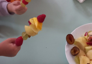 Na zdjęciu widać dzieci nabijające owoce na patyczki do szaszłyków.