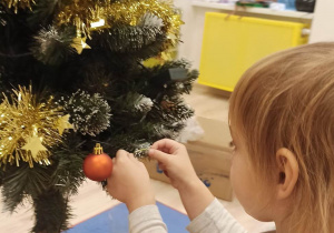 Dziewczynka wiesza bombkę na choince.