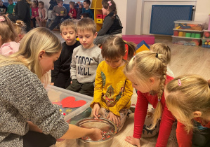 Nauczycielka wyciąga z miski z wodą wosk. Dzieci patrzą na jego kształt.