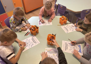 Dzieci siedzą przy stoliku i kolorują kolorowanki przedstawiające misia z książką. Na górze strony znajduje się napis: "Dzień postaci z bajek z Małym Misiem".