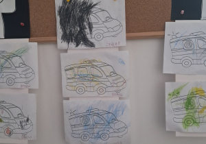 Tablica z pracami dzieci. Kolorowanki przedstawiające pojazdy policji i karetki pomalowane kredkami.