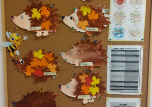 9 prac dzieci - wycięte z papieru i pomalowane jeże, na których są przyklejone papierowe, kolorowe liście