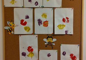 Tablica z pracami dzieci. Prace wykonane za pomocą stemplowania owocami maczanymi w farbie.