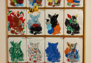 Tablica z pracami dzieci. 12 kolorowanek, pokolorowanych pastelami, przedstawiających królika z jajkiem.