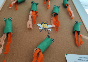 Tablica z pracami dzieci - żabki wykonane z rulonu zielonego papieru oraz bibuły.