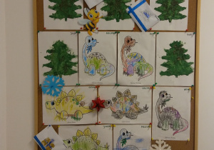 5 prac dzieci przyczepionych do korkowej tablicy. Szablony choinek pomalowane na zielono i ozdobione igłami z drzew iglastych oraz 7 kolorowanek przedstawiających dinozaury.