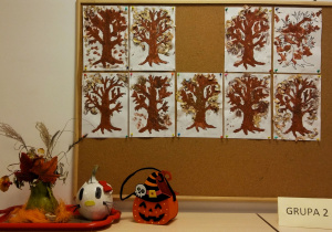 Tablica z pracami dzieci: szablony drzew pomalowane farbą oraz ozdobione obierkami z kredek ołówkowych.