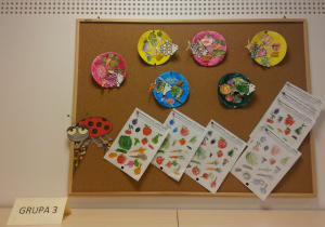 Tablica korkowa z pracami dzieci - karty pracy oraz pomalowane papierowe talerzyki, do których zostały przyklejone papierowe, pokolorowane obrazki zdrowych produktów spożywczych