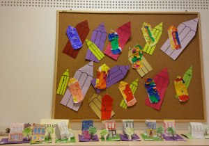 Tablica z pracami dzieci, Prace wykonane z okazji Dnia Kredki - szablony kredek ozdobione bibułą. Tło stanowią kolorowe kredki wycięte z papieru.