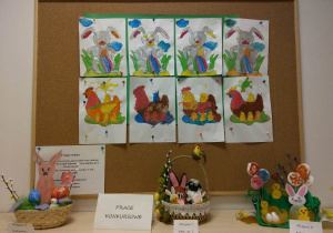 Tablica z pracami dzieci. Pomalowane farbami obrazki przedstawiające królika z pisanką lub kurę z kurczaczkami.