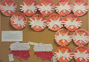 Tablica z pracami dzieci. Na tablicy znajdują się repliki godła: pomalowane farbami na czerwono talerzyki, na których znajdują się białe "orły" wykonane z odrysowanych dłoni dzieci. Na dole znajdują się dwie prace zbiorowe: kształt Polski wyklejony kulkami z bibuły w kolorach flagi narodowej.