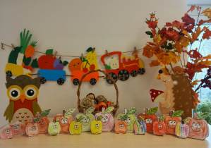 Jesienny kącik przyrodniczy oraz prace plastyczne dzieci - wycięte z papieru, pokolorowane, stojące na półce jabłka