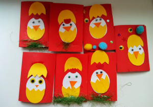 Na zdjęciu znajdują się wielkanocne kartki wykonane przez dzieci. Na czerwonych kartkach przyklejono wyciętego z papieru kurczaka wychodzącego z pękniętego jajka. Niektóre prace ozdobiono dodatkowo pomponikami, naklejkami oraz zielonym siankiem.