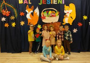 Dzieci z grupy Biedronek pozują na tle jesiennych dekoracji i napisu Bal Jesieni